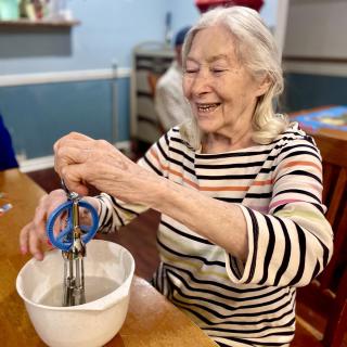 An elderly woman joyfully mixing ingredients in a kitchen.