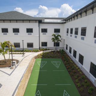 A modern building with a courtyard featuring a shuffleboard court surrounded by landscaped greenery.