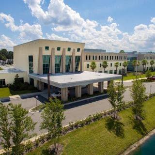 A modern hotel building with a welcoming entrance, surrounded by lush greenery and under a bright sky.