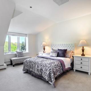 A bright and spacious bedroom featuring a large bed with patterned bedding, flanked by two nightstands with lamps, and a window letting in natural light.