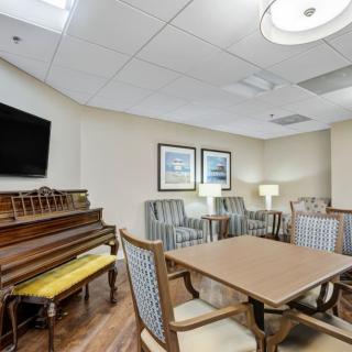 A cozy room featuring a piano, table with chairs, a television, and artwork on the walls.