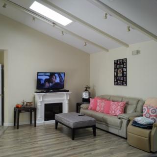 A cozy living room with a sofa, television, and fireplace beneath a vaulted ceiling with skylights.