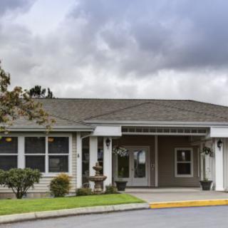 A single-story residential building with a covered entrance and surrounded by landscaping under a cloudy sky.