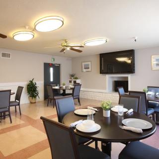 A modern dining room with neatly arranged tables and chairs, featuring contemporary lighting and a large television.