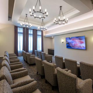 A modern conference room with comfortable seating, chandeliers, and a large television screen.