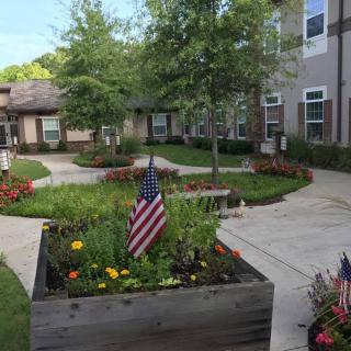 A peaceful courtyard garden with American flags, flowers, and pathways surrounded by buildings.