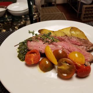 A beautifully plated roast beef accompanied by colorful roasted vegetables and herbs.