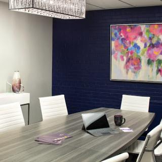 A stylish modern meeting room featuring a large conference table, white chairs, and vibrant artwork on the wall.