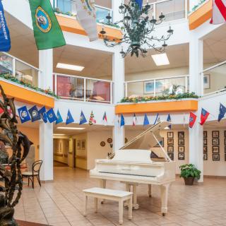 A brightly lit atrium featuring a white grand piano and surrounded by various flags hanging from the balcony.