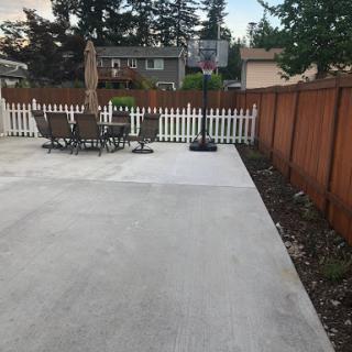 A spacious outdoor patio area featuring a basketball hoop and seating arrangements, enclosed by a wooden fence.
