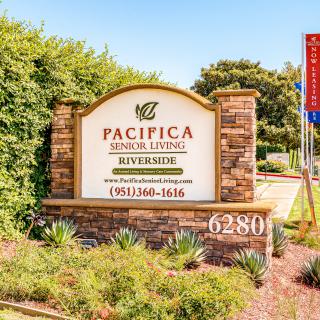 Entrance sign for Pacifica Senior Living Riverside surrounded by landscaping.