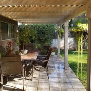A cozy patio with outdoor furniture under a pergola, surrounded by a lush garden.