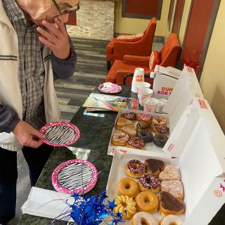 A person choosing from a variety of donuts on a table.