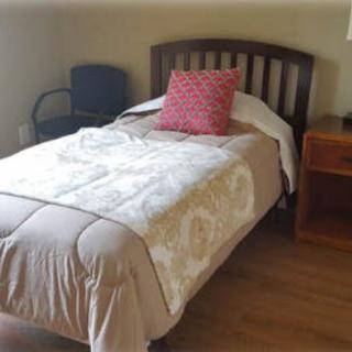 A simple bedroom with a single bed, a colorful pillow, a nightstand, and a chair.