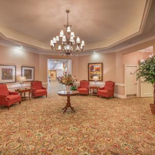 A warmly decorated lobby featuring a large chandelier, red upholstered chairs, and elegant artwork on the walls.