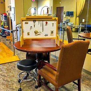 A rehabilitation therapy room featuring a round table with occupational therapy tools displayed on a board.