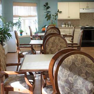 A cozy dining area with elegant chairs and tables, featuring indoor plants and a view of the kitchen.