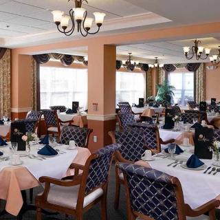 An elegant dining room with neatly arranged tables and chairs, featuring chandeliers and natural lighting.