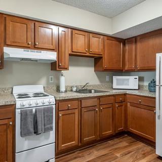 A modern kitchen with wooden cabinets, a stove, microwave, sink, and refrigerator.