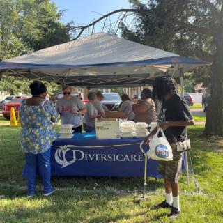 People gather at an outdoor community event under a tent labeled 'Diversicare'.