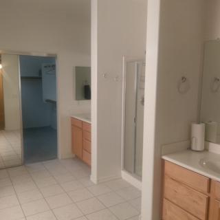 A spacious bathroom featuring two sinks, a shower, and wooden cabinets.