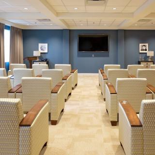 A modern conference room with rows of upholstered chairs facing a large television screen.