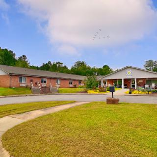 A view of a residential building surrounded by green grass and trees under a partly cloudy sky.