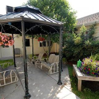 A charming garden patio with a gazebo and outdoor seating surrounded by lush greenery and flowers.