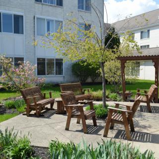 A peaceful garden with wooden seating and a pergola next to an apartment building.