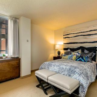 A modern bedroom with stylish decor featuring a large bed, abstract artwork above the headboard, and a window letting in natural light.