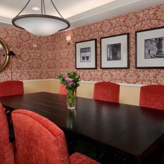 A stylish dining room with red upholstered chairs and a dark wooden table, complemented by patterned wallpaper and framed photos on the wall.