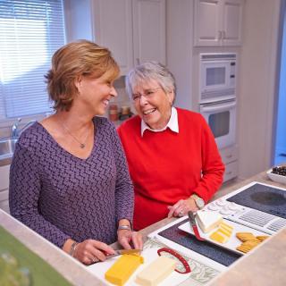 Two women smiling and preparing food together in a kitchen.