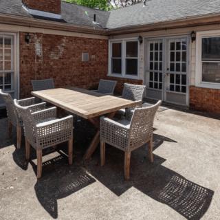 Outdoor patio area with a wooden table and wicker chairs set against a brick wall backdrop.