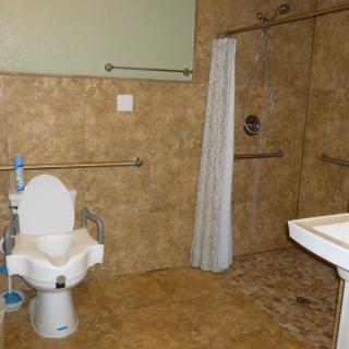 An accessible bathroom with handrails, a shower area, and a toilet seat designed for wheelchair users.