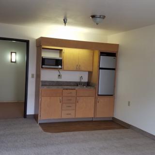 A compact kitchenette in an apartment with wooden cabinets and a small fridge.