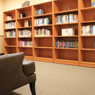 A cozy library corner with a large wooden bookshelf filled with books, and an armchair in the foreground.
