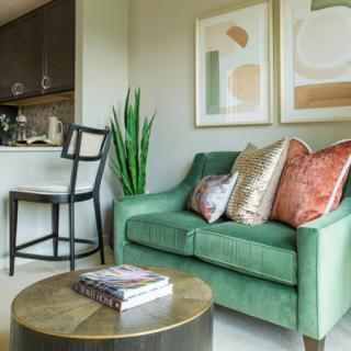 A cozy living room with a green sofa, decorative pillows, abstract artwork, and a small plant beside a stylish coffee table.