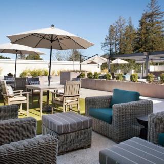 A spacious outdoor patio with wicker furniture, including chairs, tables, and umbrellas under a clear blue sky.