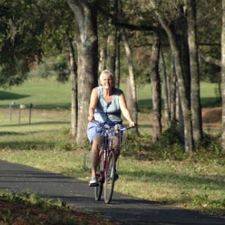 A woman enjoying a leisurely ride on her bicycle along a scenic path surrounded by trees.