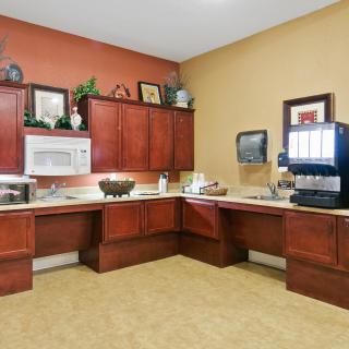 A modern kitchen area with wooden cabinets, equipped with a microwave and coffee machine.