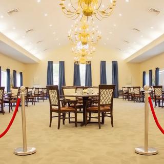 A spacious and elegantly designed dining room featuring chandeliers, neatly arranged tables and chairs, and decorative curtains.