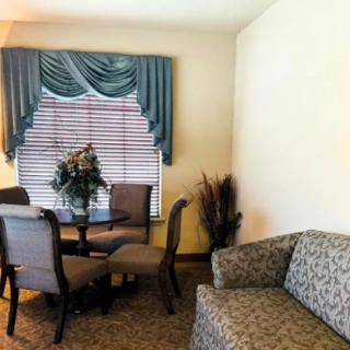 A cozy living room setup with a sofa, a round table surrounded by chairs, and a window with draped curtains.