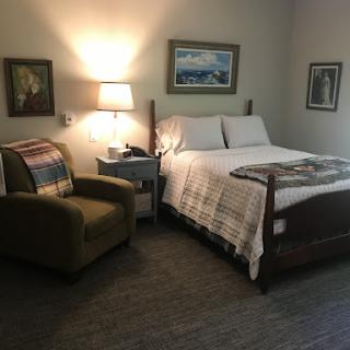 A cozy bedroom setup featuring a comfortable bed, an armchair, and artistic wall decor.