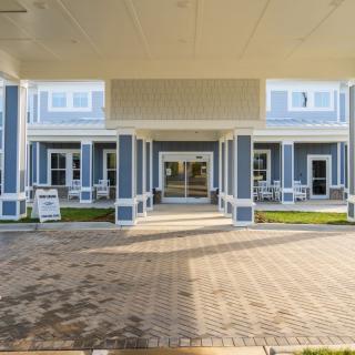 A view of a building entrance with a covered driveway and patio seating.