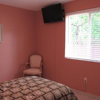 A cozy bedroom with pink walls, a chair, and a wall-mounted television.