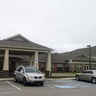 A view of a residential building with cars parked in front under a cloudy sky.