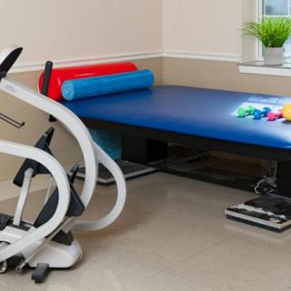 A physical therapy room with equipment including a treatment table, fitness rollers, and small dumbbells.