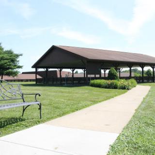 A sunny day at the park featuring a pavilion and a pathway lined with greenery.