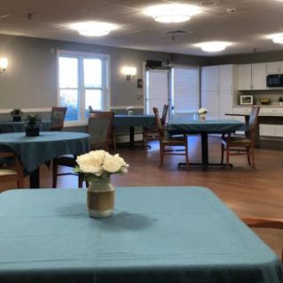 A communal dining area with tables and chairs, featuring a kitchen and decorative flowers on the tables.