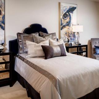 A stylishly decorated bedroom with a bed adorned with multiple pillows, bedside tables, and artwork hanging on the walls.